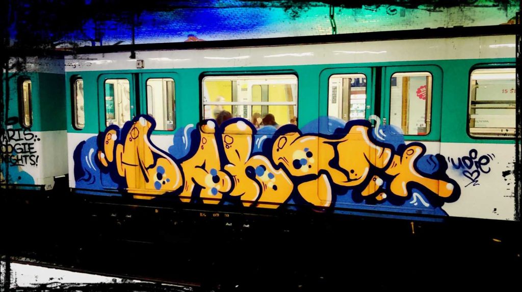 Die urbane Kultur leistet einen wichtigen Beitrag zum Lebensgefühl von Urbanität. Im Bild ist ein oranges Graffiti mit blauem Hintergrund auf einer U-Bahn von Paris zu sehen.